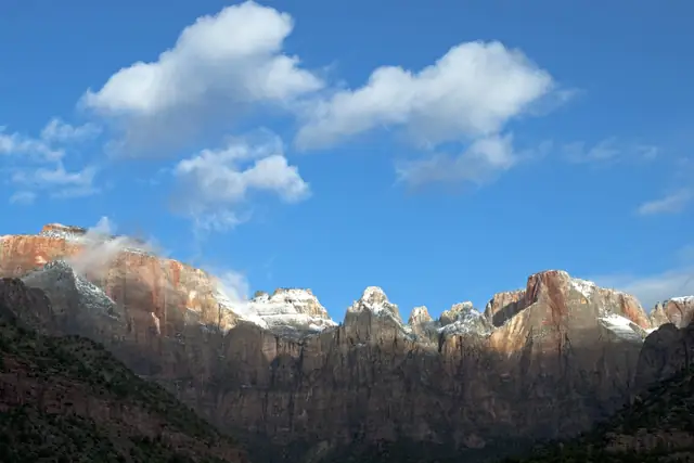 A spring dusting of snow on the peaks above Zion Canyon under white clouds.