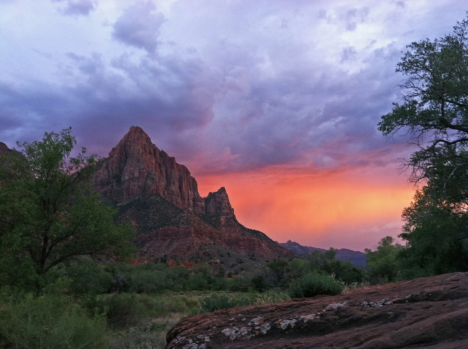 The Watchman peak in silhouette under an orange and purple stormy sunset sky, Zion National Park.
